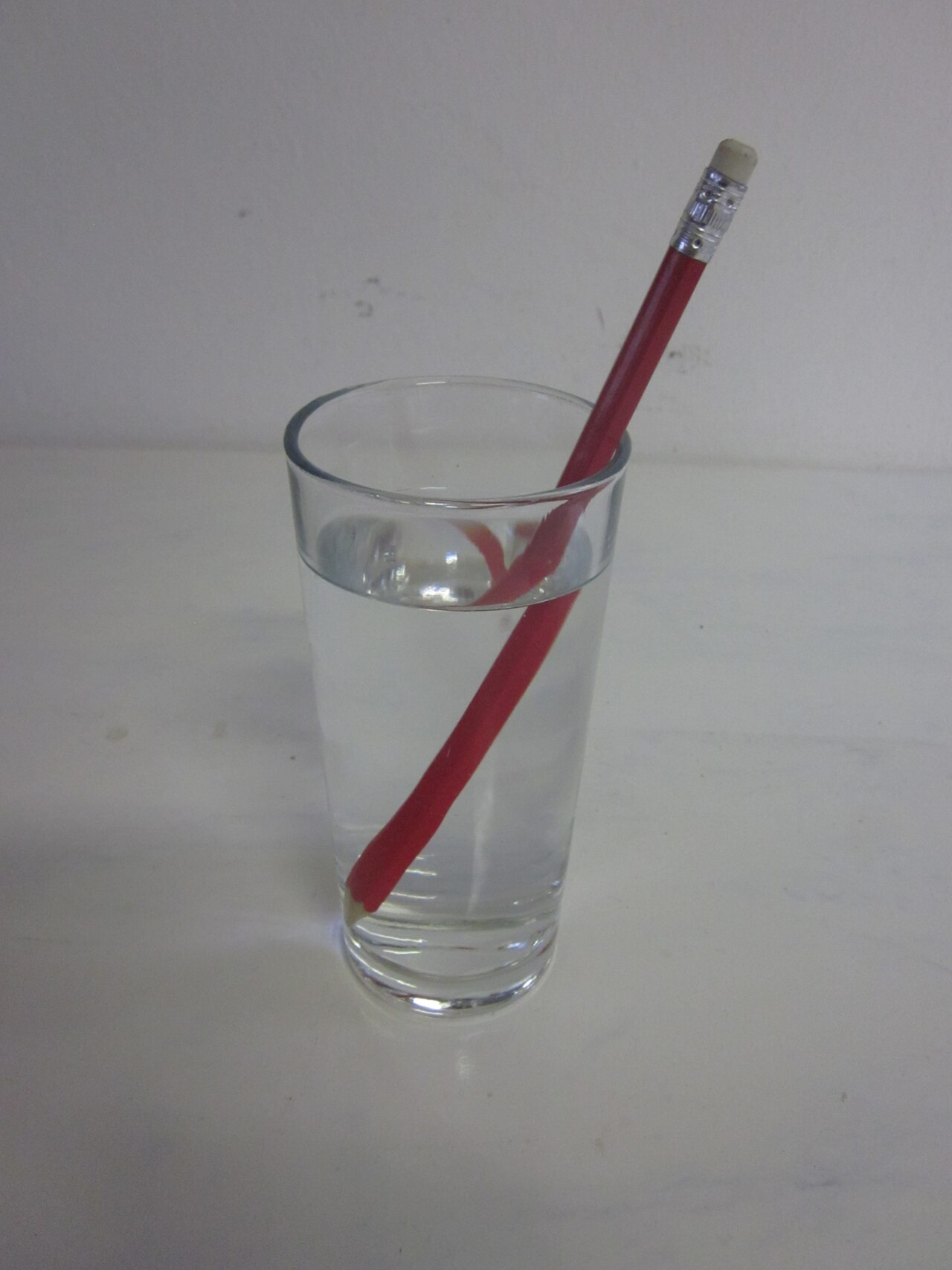 A pencil standing in a glass of water appears bent and shifted at the surface