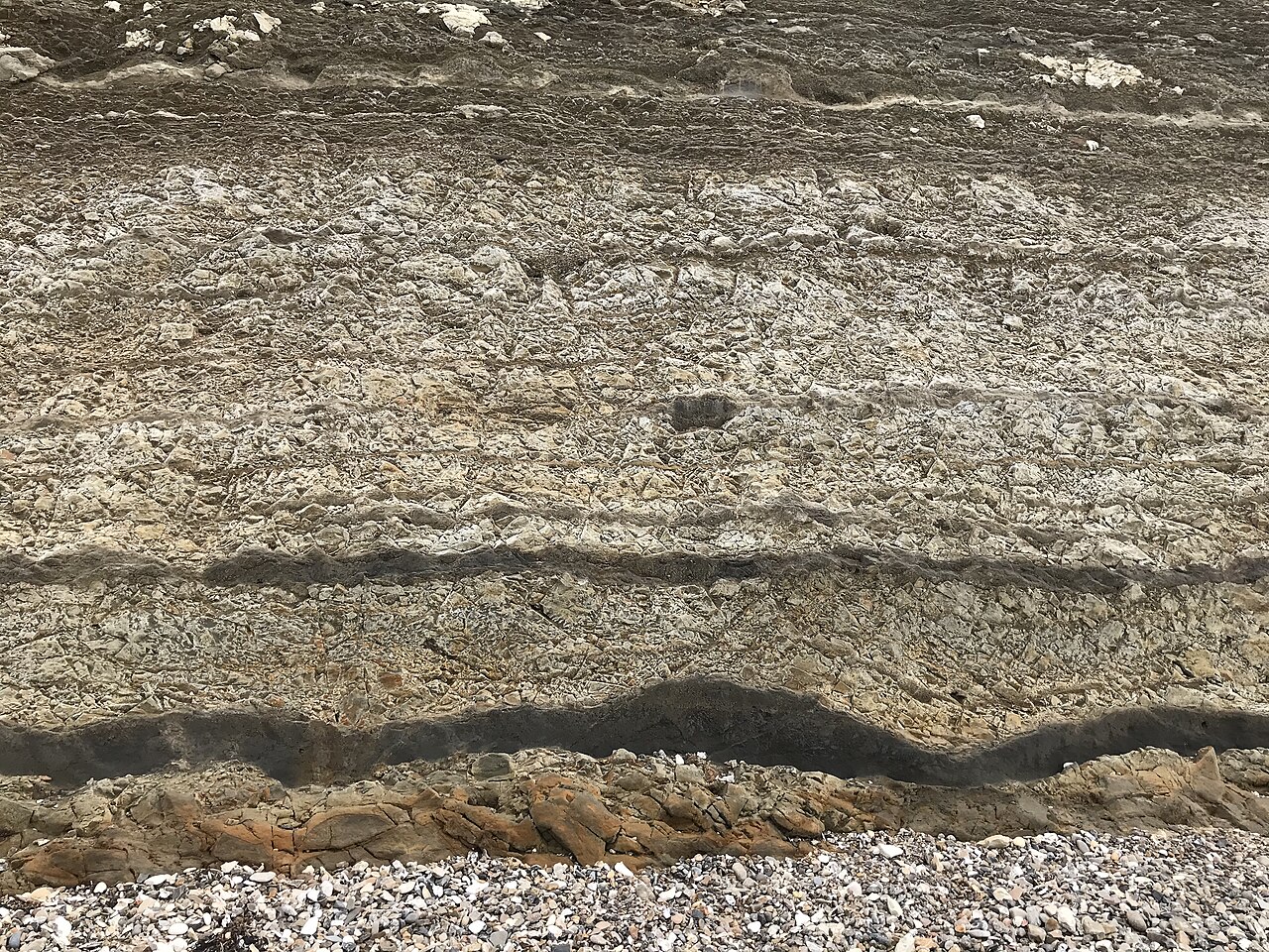 A cliff face made of neat horizontal bands of pale rock separated by darker stripes of volcanic ash