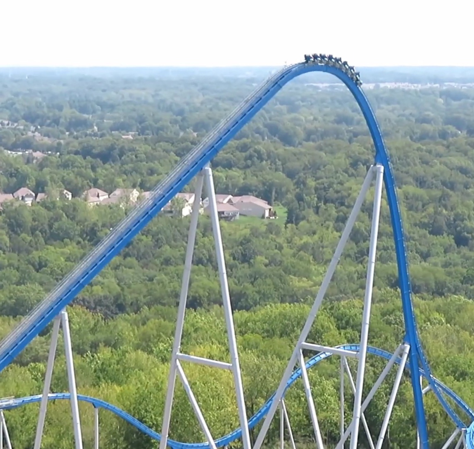 A rollercoaster train cresting the top of a tall hill just before the steep drop