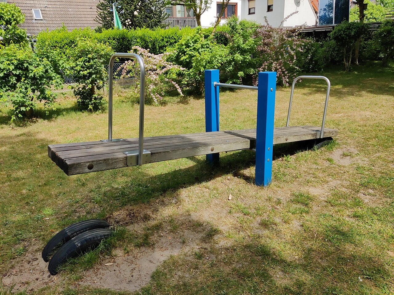 A wooden playground seesaw balanced on a central pivot post, with a handle at each end