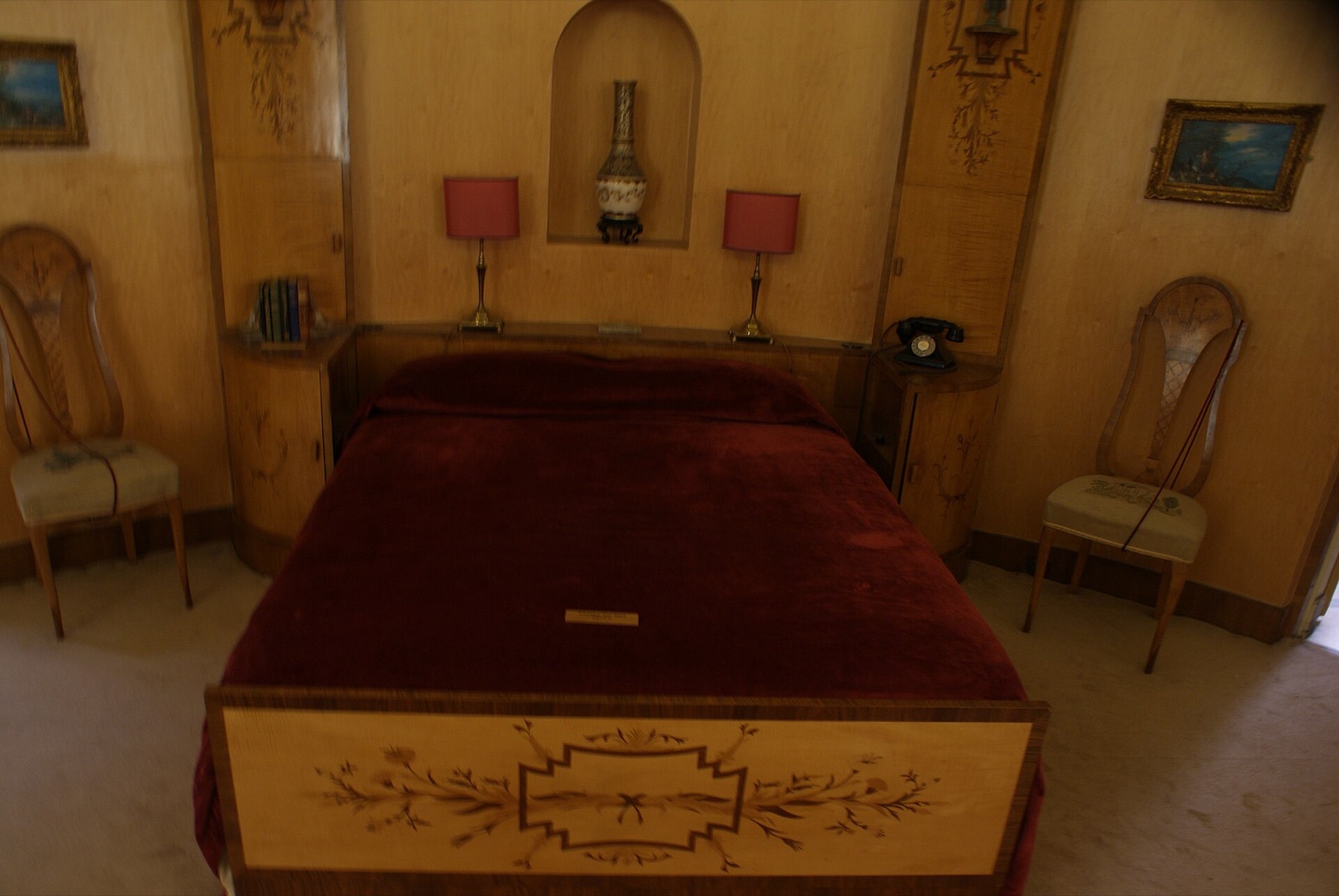 A neatly made bed with a deep red cover in a quiet bedroom, ready for a night’s sleep.