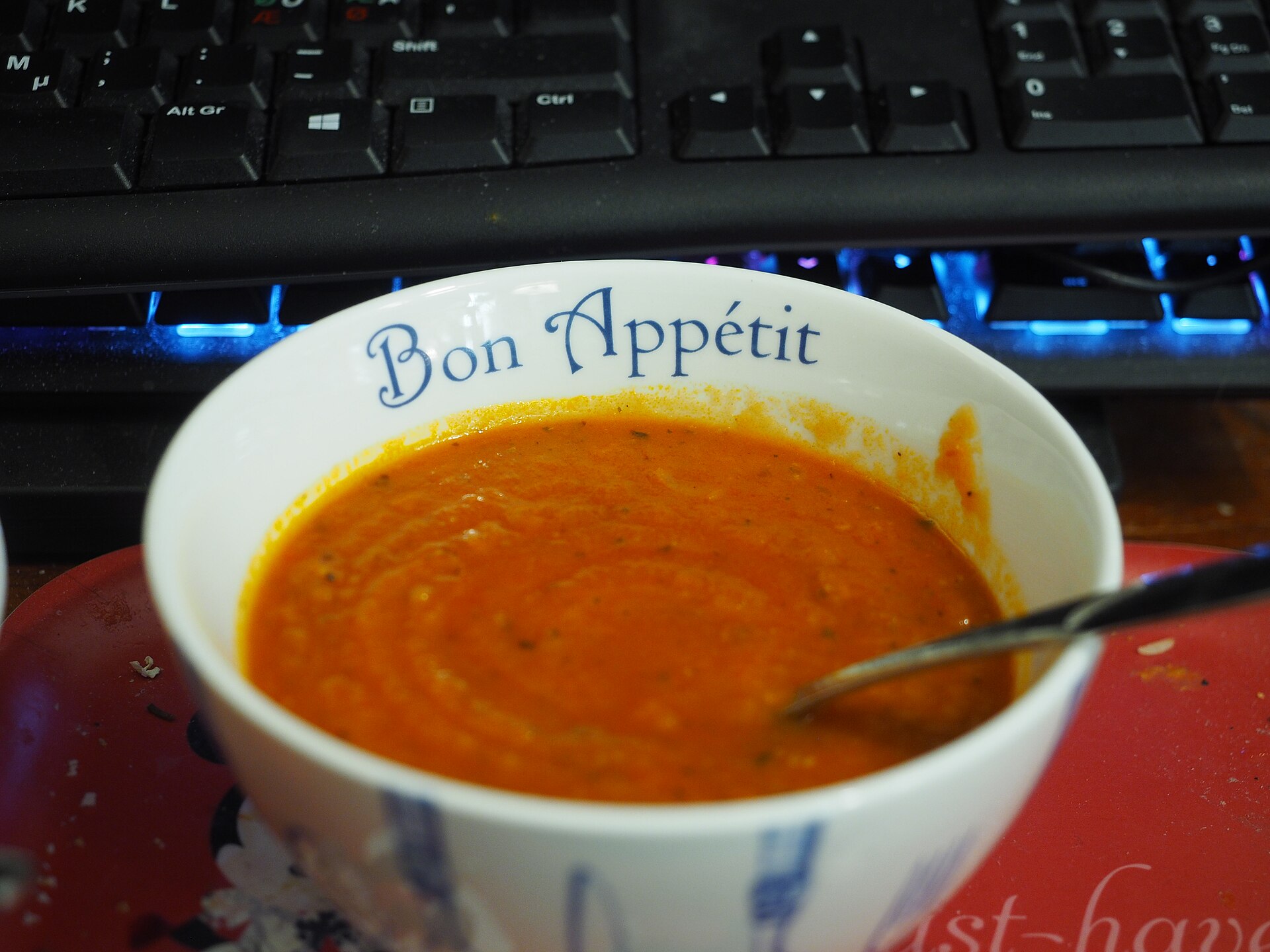 A bowl of hot orange tomato soup with a spoon resting in it