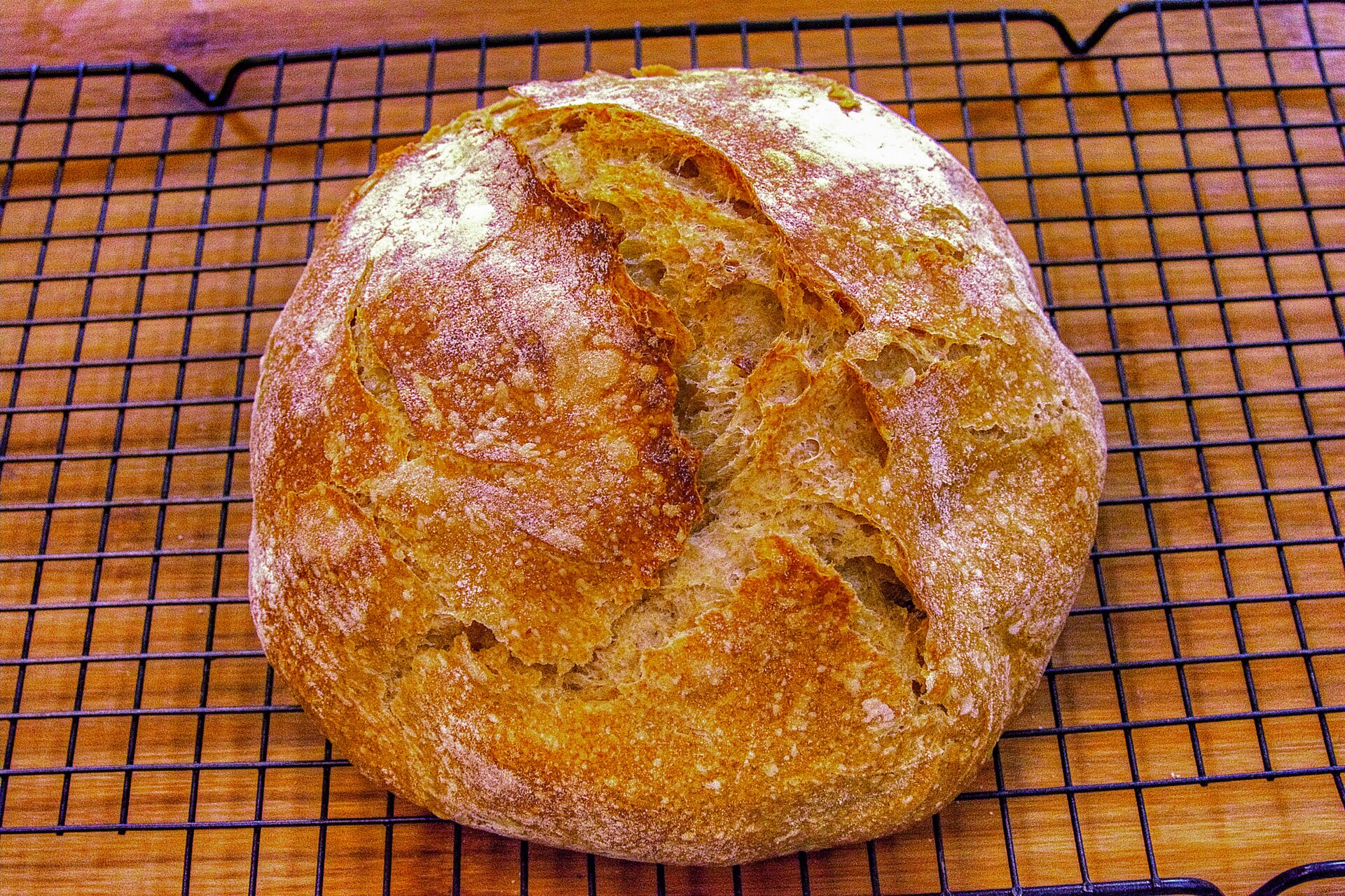 A round golden loaf of freshly baked bread cooling on a wire rack