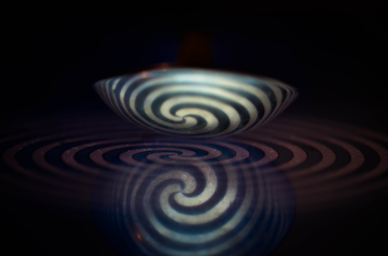 A spiral pattern reflected and distorted in the curved, shiny bowl of a spoon.