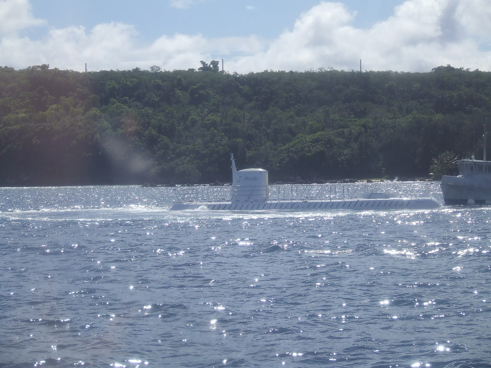 A white tourist submarine at the surface of the sea, its conning tower and deck showing above the water.