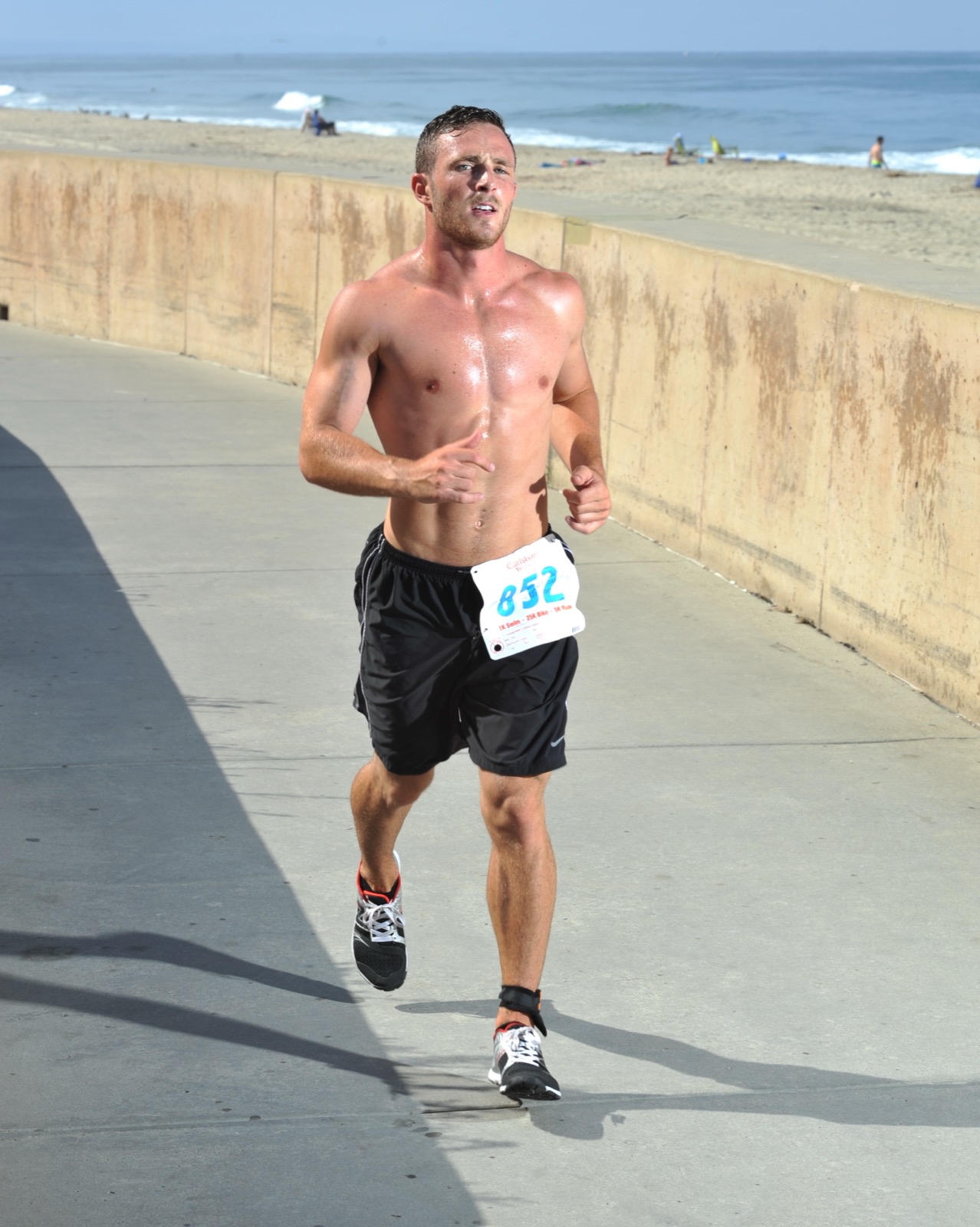A runner in a race glistening with sweat on a sunny day by the sea.