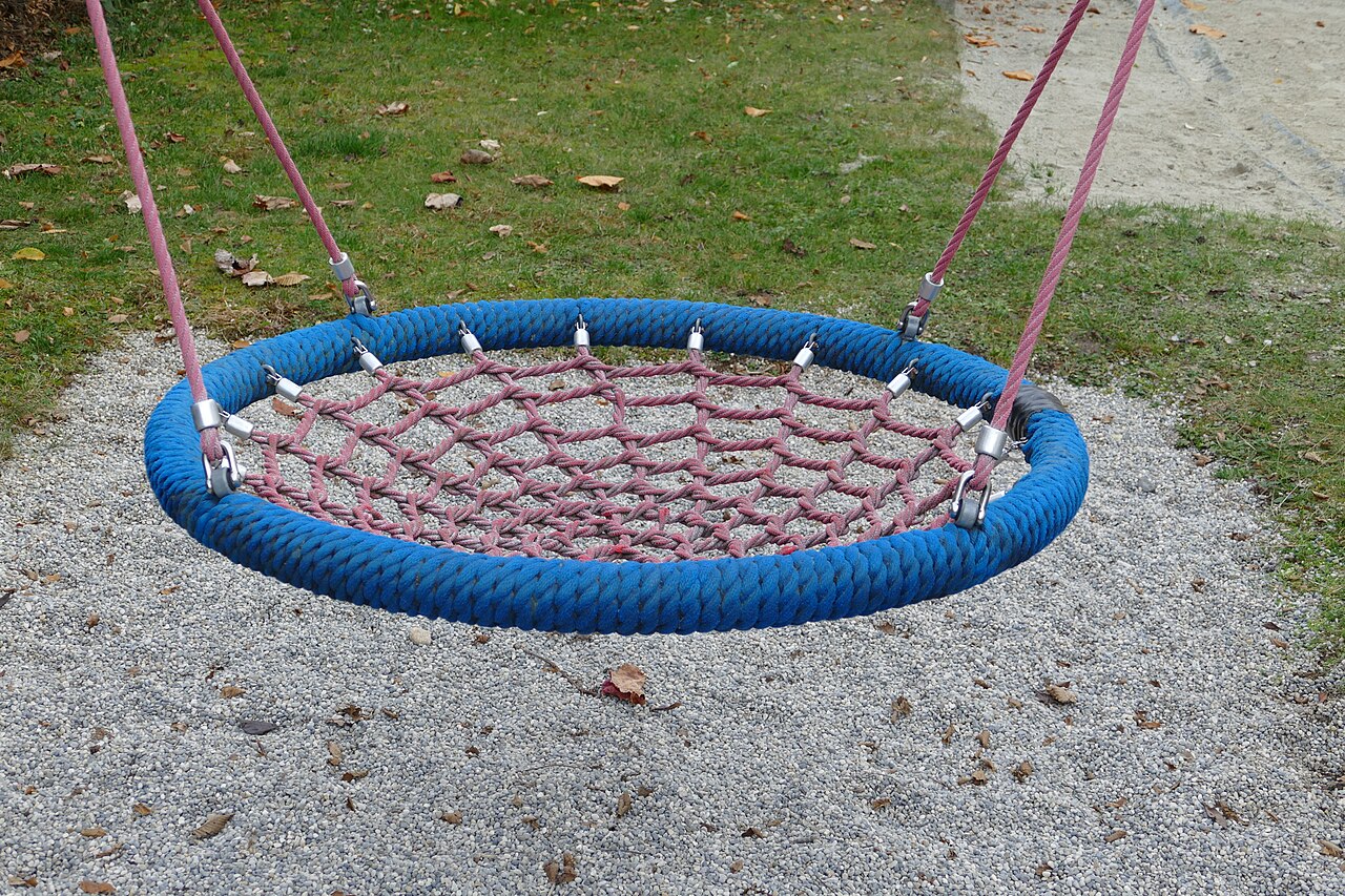 An empty round nest swing hanging still from long ropes above a playground