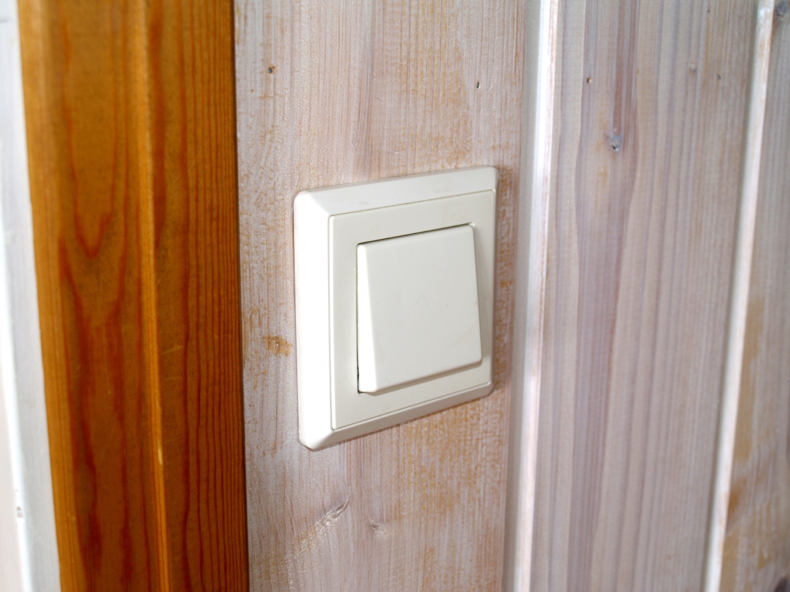 A white wall light switch mounted on wooden panelling