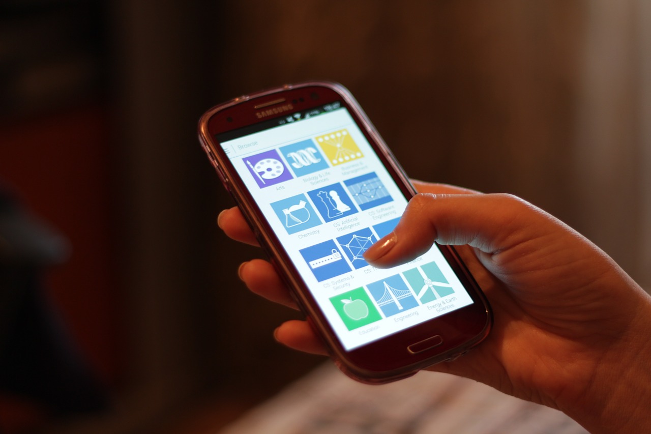 A hand holding a phone with a thumb reaching across to tap one of the coloured squares on the screen