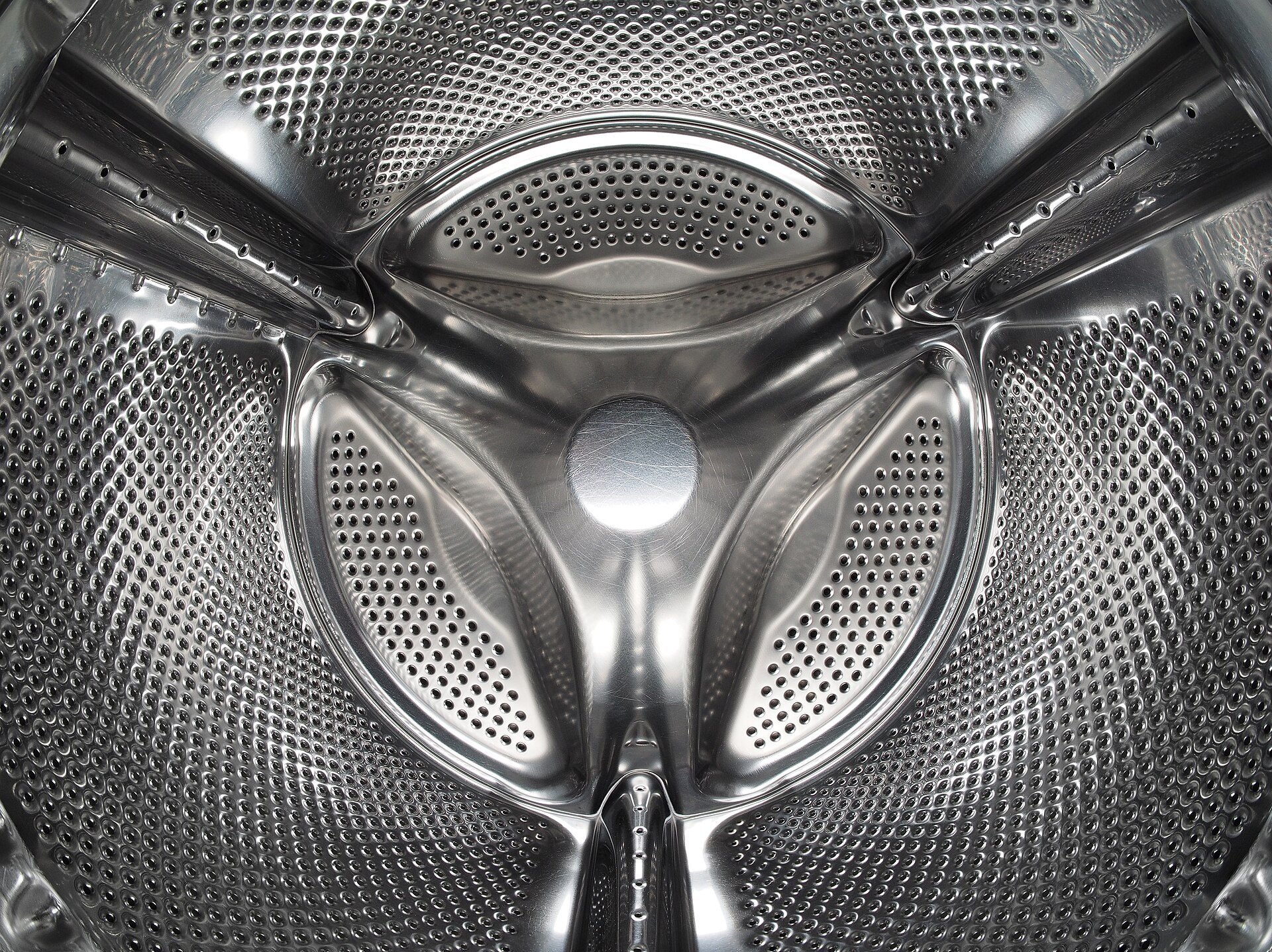 A close-up inside a stainless steel washing machine drum, its curved wall covered in thousands of small holes.