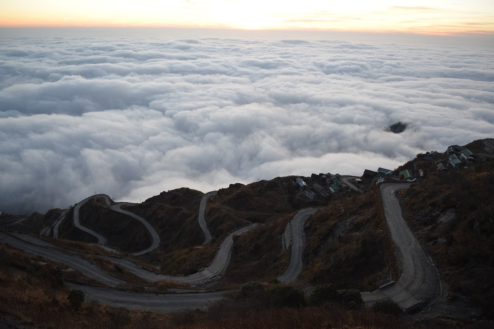A road winding in tight hairpin bends down a mountainside above the clouds.