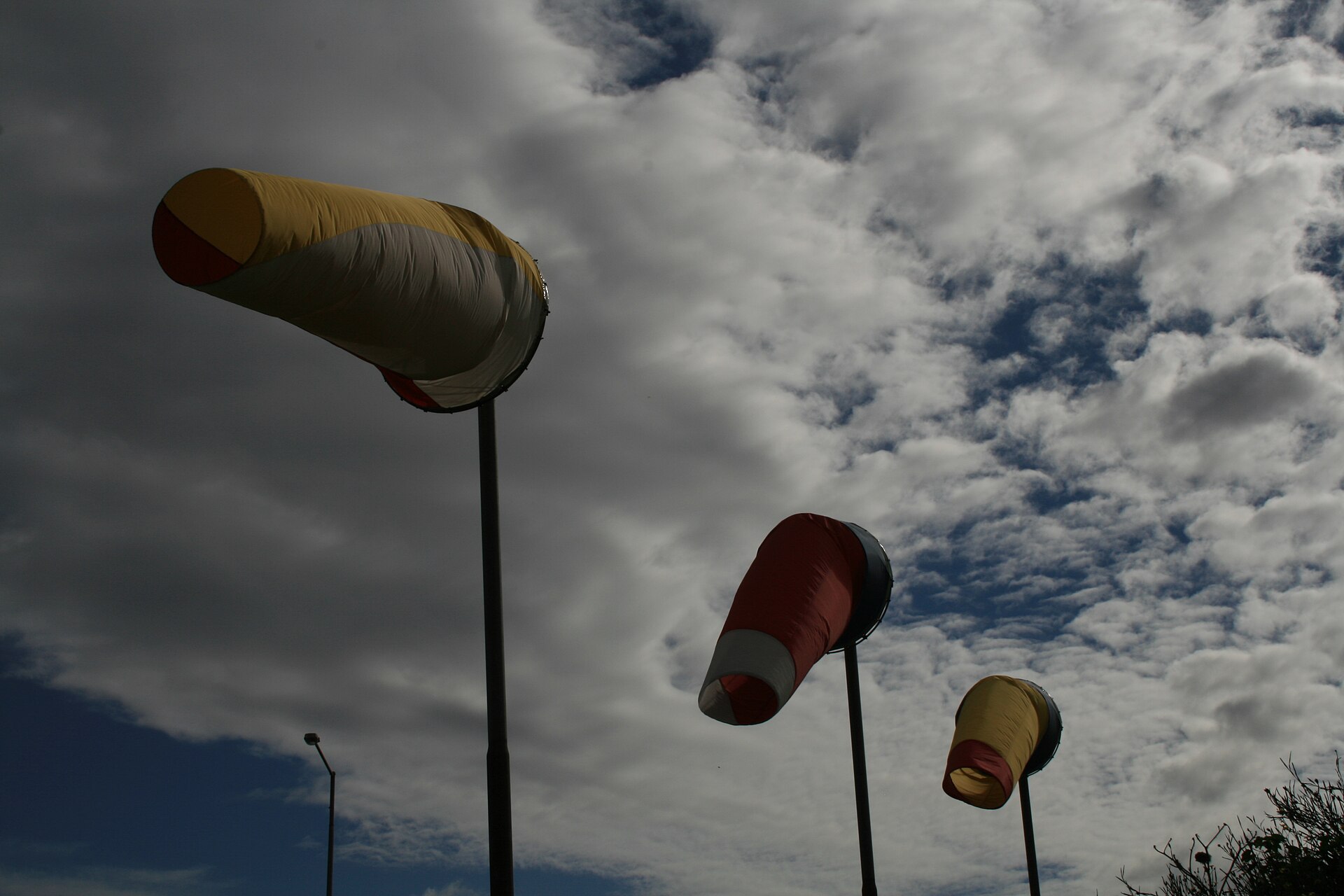 Three windsocks filled and streaming sideways in a strong breeze against a cloudy sky