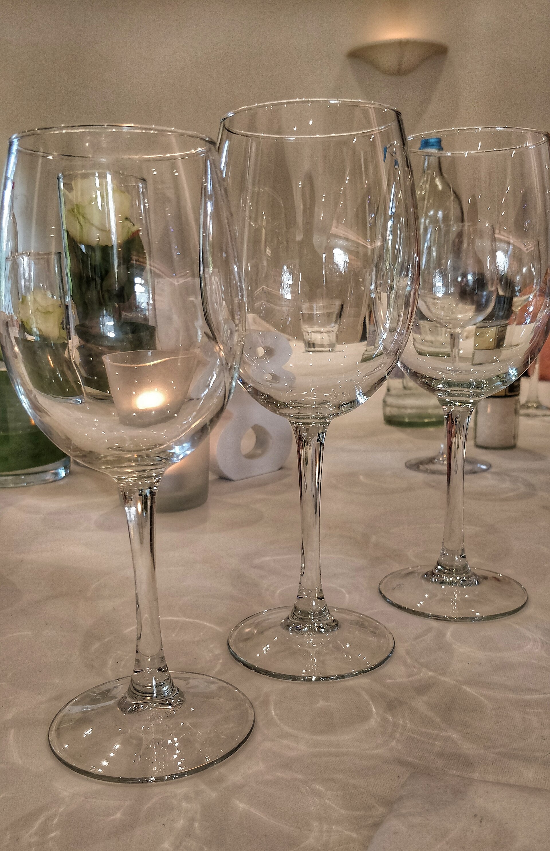 Three thin-stemmed wine glasses standing empty on a white tablecloth, catching the light.